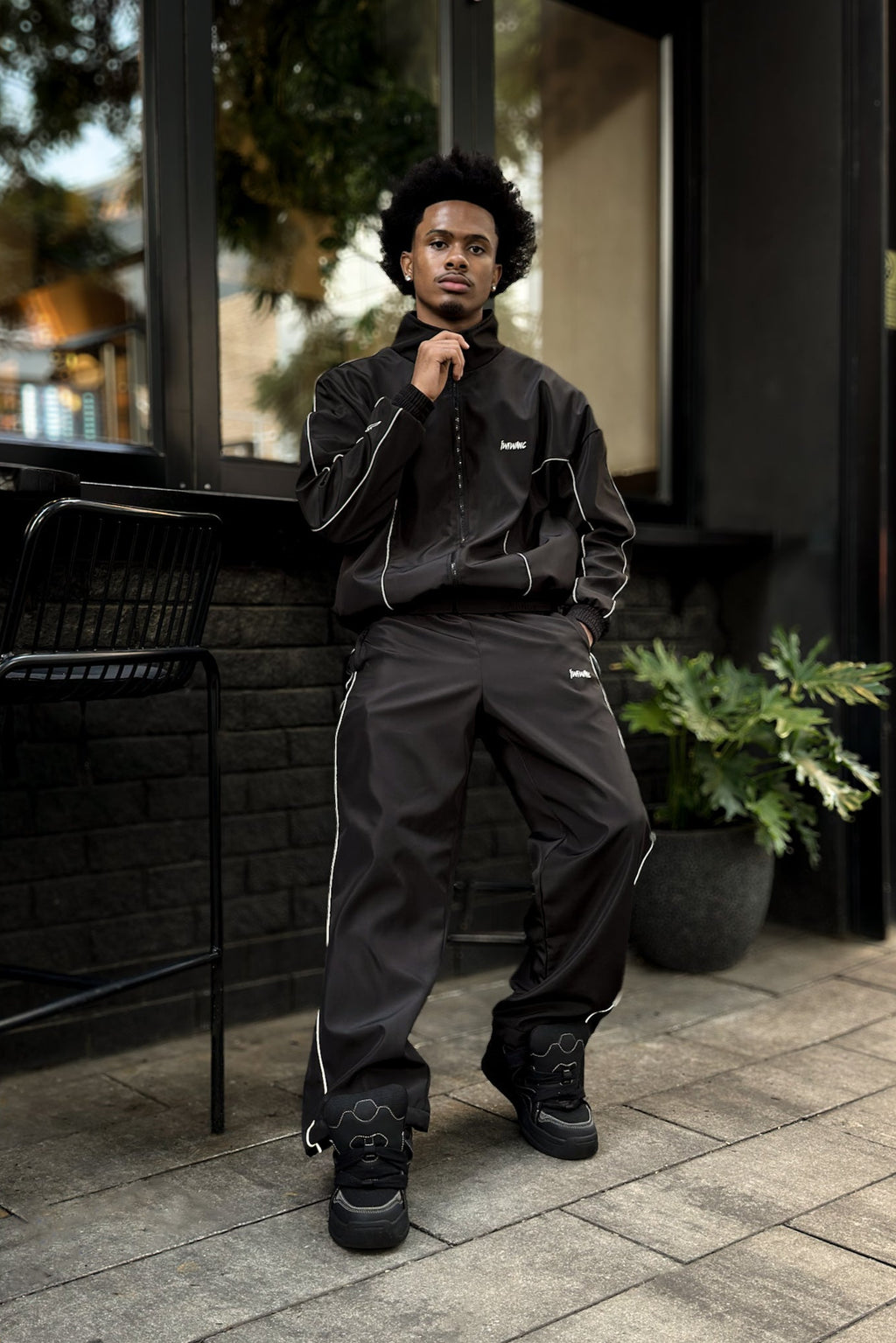 Person wearing a black tracksuit standing outdoors on a patio.

