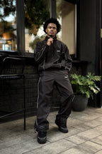 Person wearing a black tracksuit standing outdoors on a patio.


